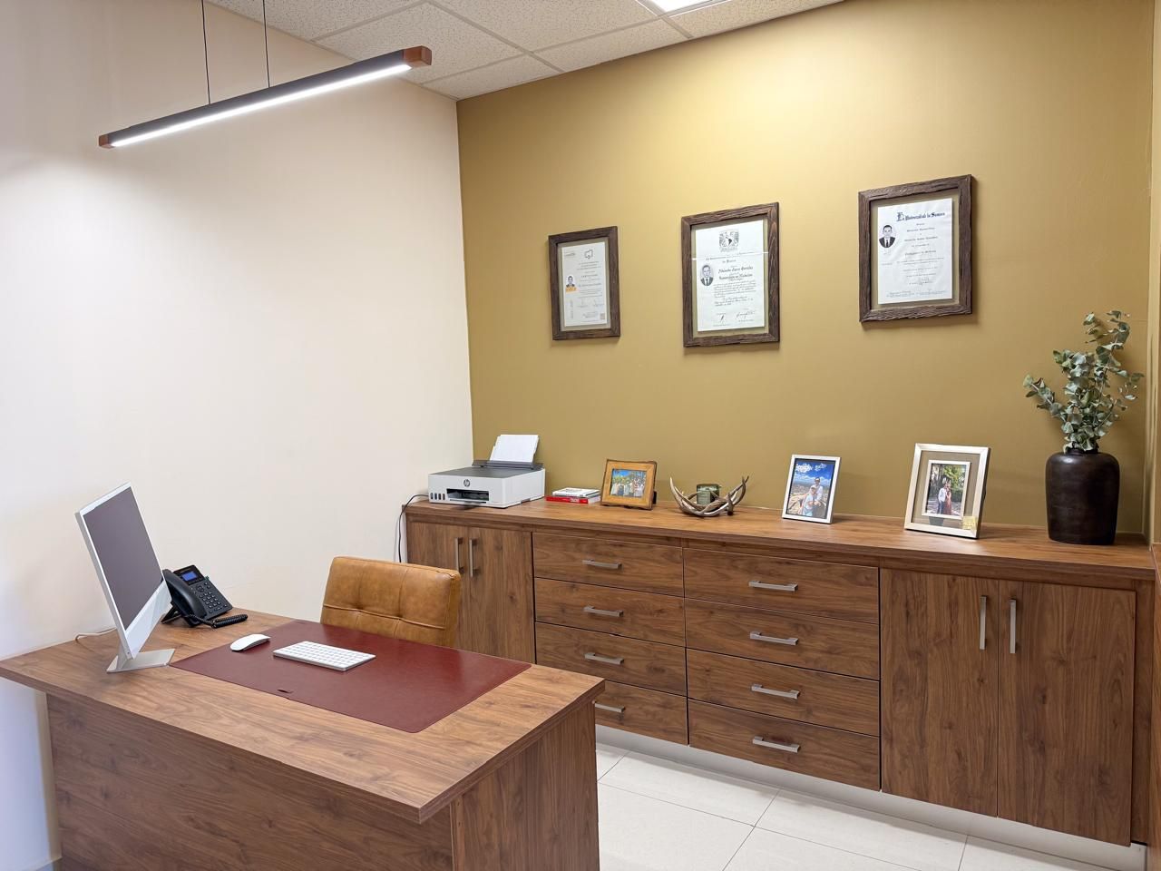 Despacho del consultorio, con escritorio de madera y diplomas enmarcados en la pared